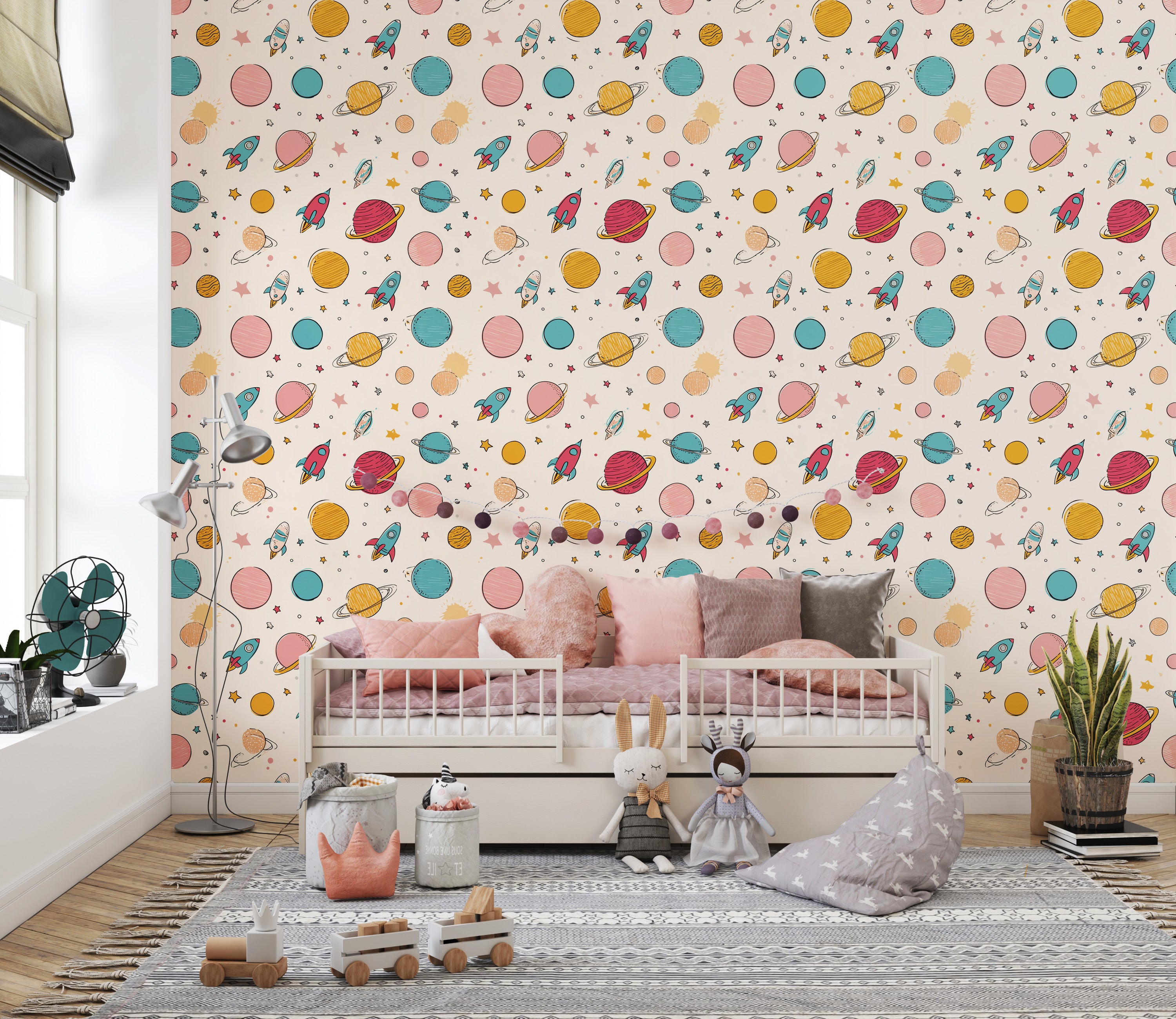 Pastel space adventure wallpaper with planets, rockets and stars on a kids' room wall behind a white bed with pink cushions a